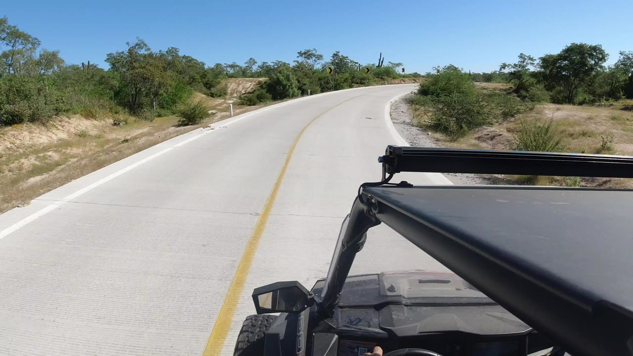 Open vehicle approaching a curving concrete road with desert shrubs.