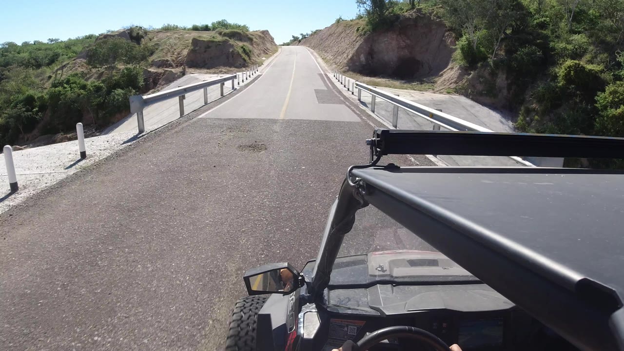 Vehicle POV turning slightly onto a bridge between rocky hillsides.