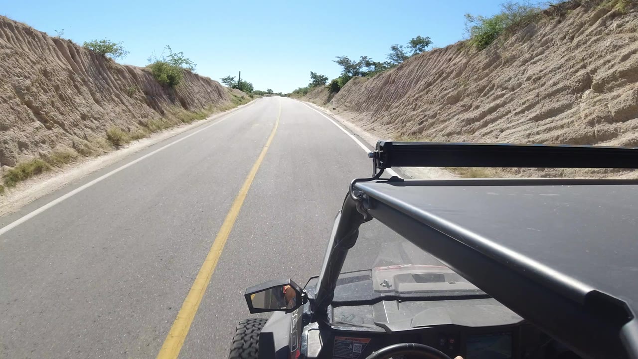 Roadway curving gently between sandy banks and sparse green shrubs.