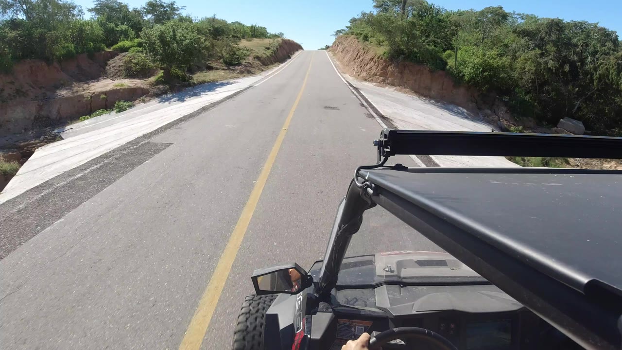 Forward view from a Jeep on a paved rural road with brush and cut banks.