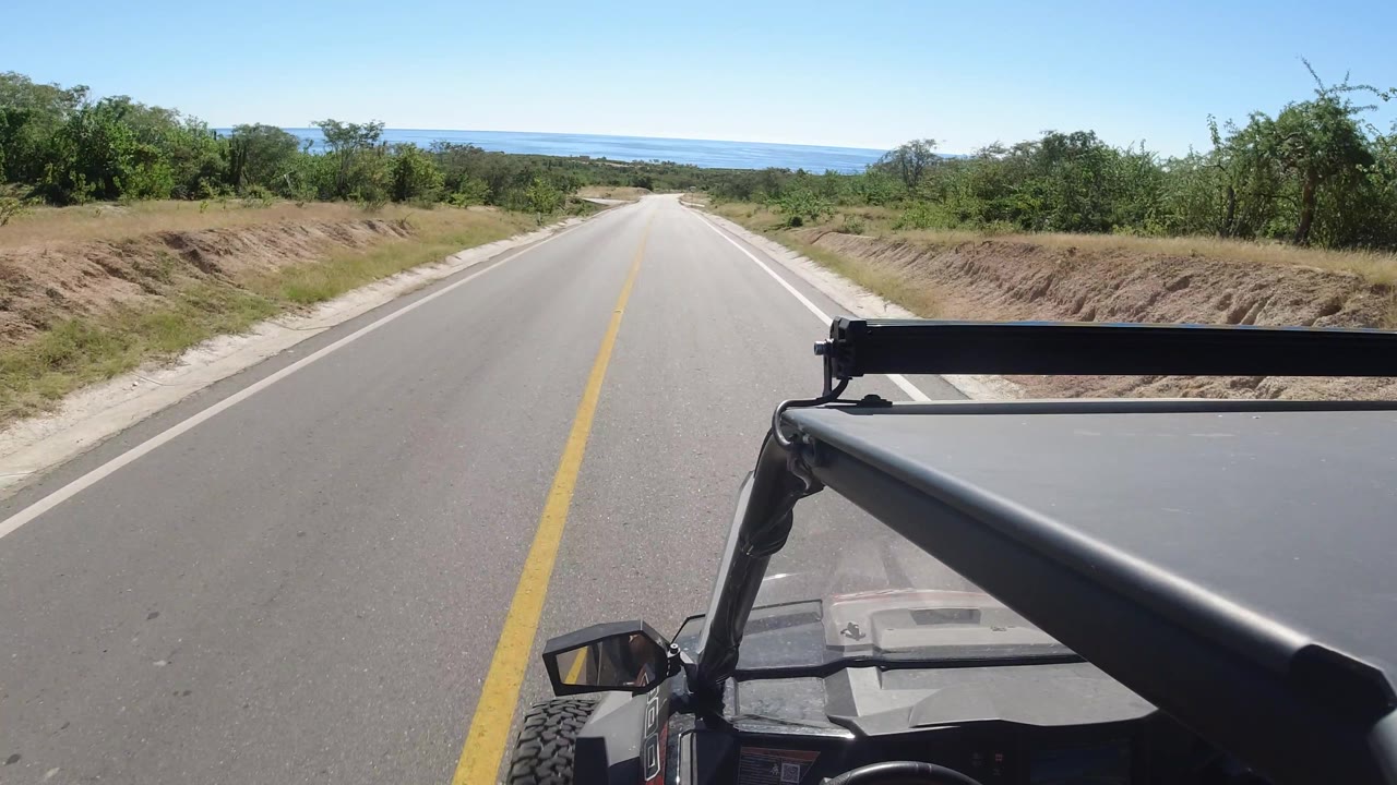 Open road descending toward distant water with vehicle hardware in foreground.
