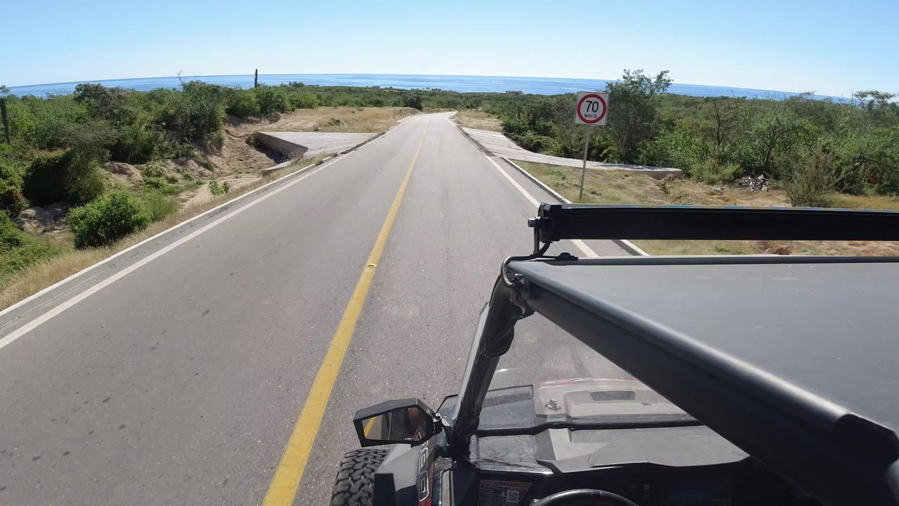 Two-lane road descending toward a distant blue sea with vehicle hardware in the foreground.