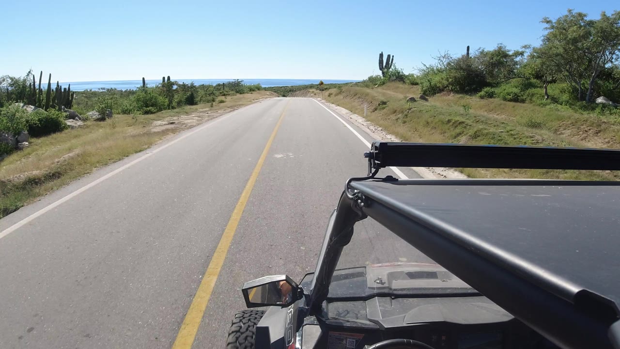 Open road curves gently past shrubs and cacti toward blue water