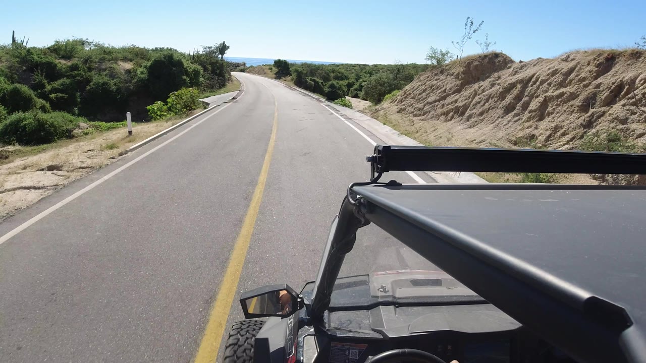 Open road with desert scrub and ocean horizon ahead.