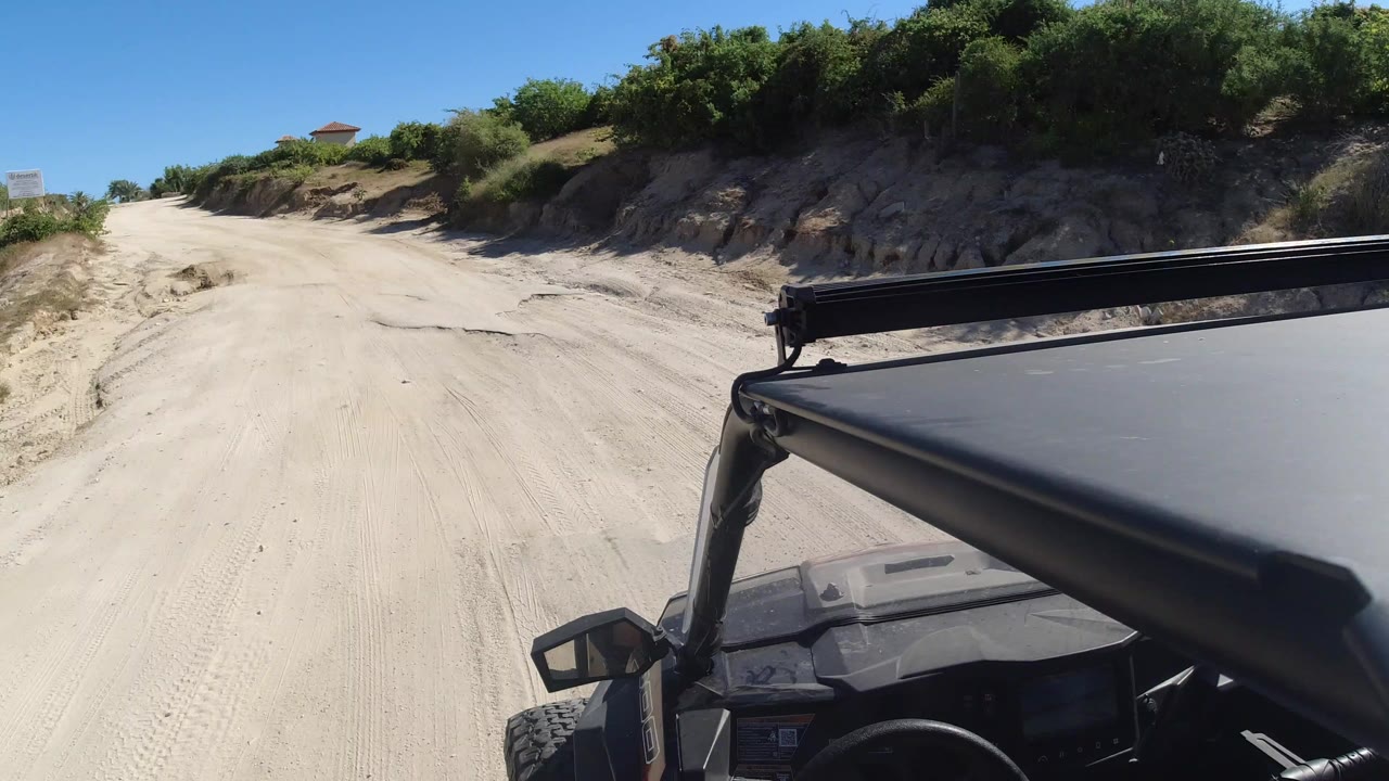 Sandy road seen from a small off-road vehicle with shrubs on both sides.