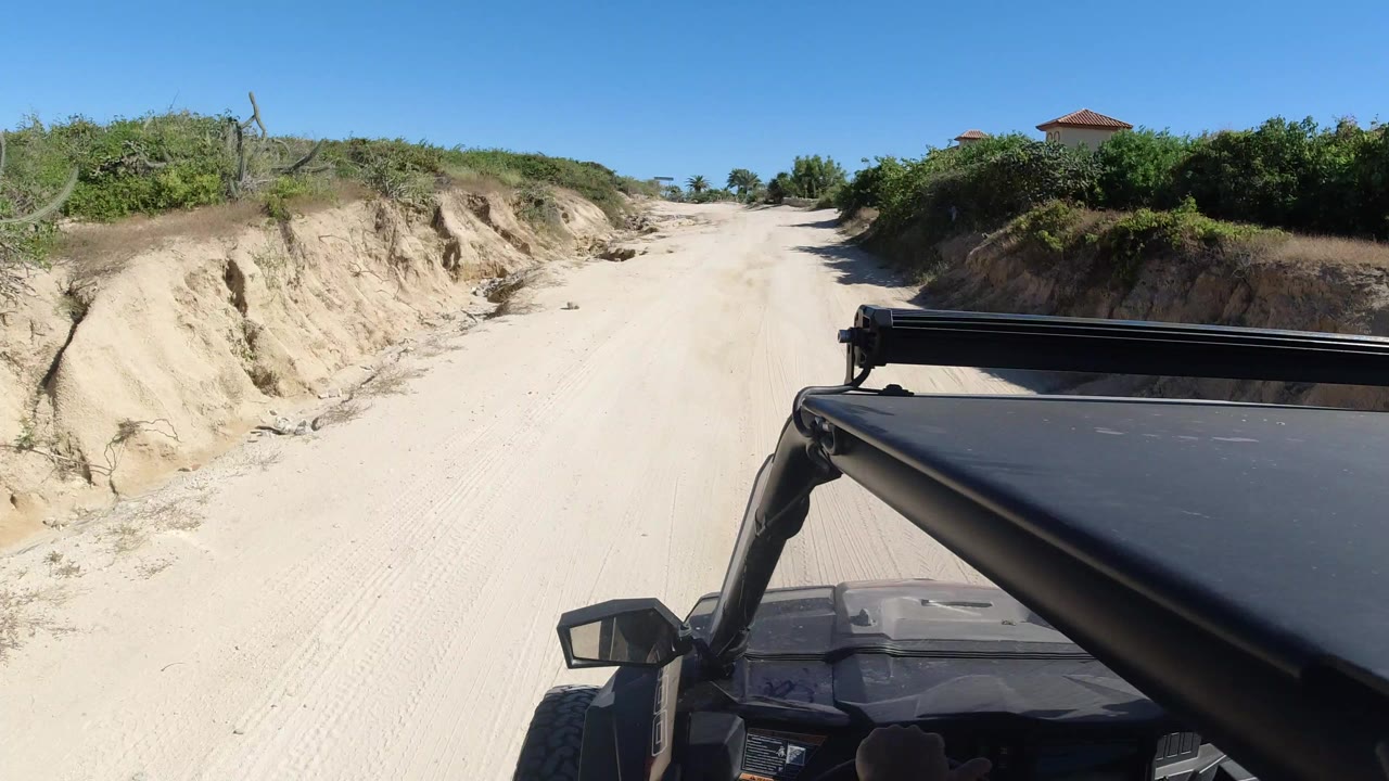 SUV foreground on a sandy dirt road between scrub-covered banks.