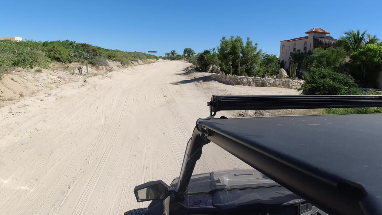 Jeep hood and light bar facing a sandy road between low bushes