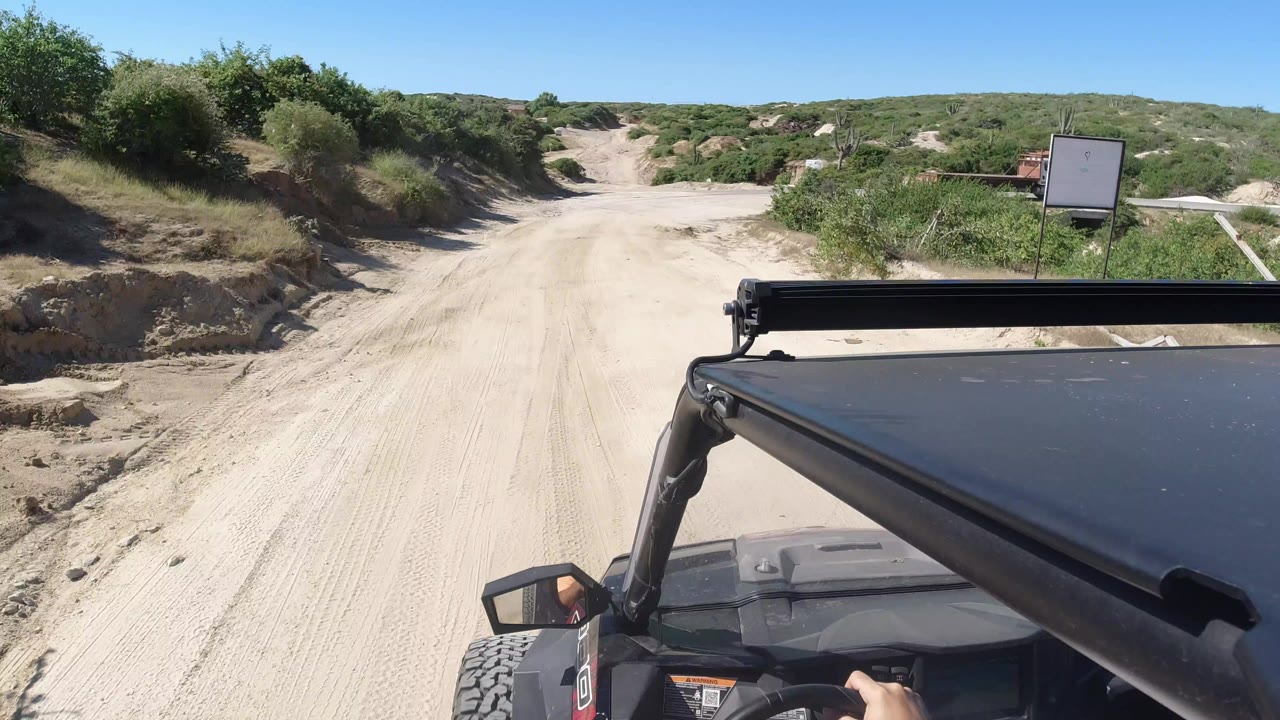 Off-road vehicle roof facing a sandy road and green scrub hills.