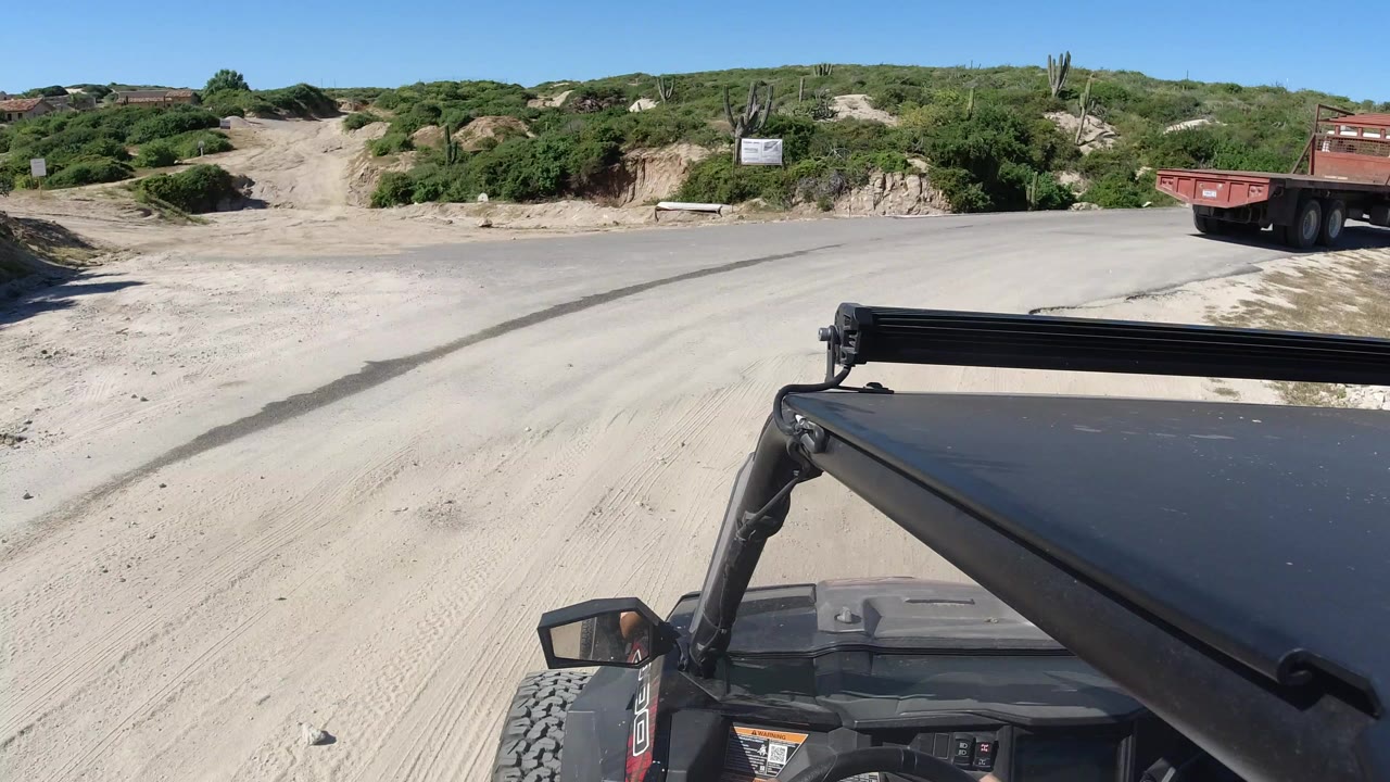 Off-road vehicle POV facing a sandy road, scrub, signs, and blue sky.