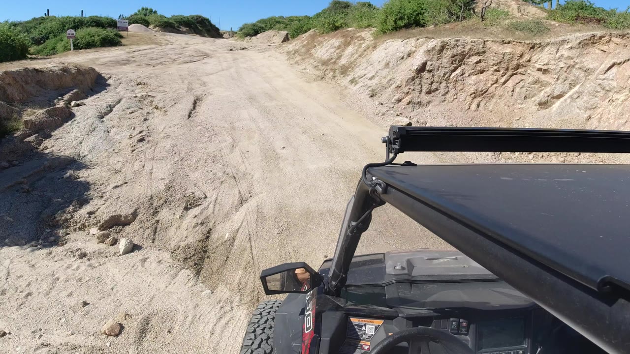 Off-road vehicle foreground on a dry dirt track with scrub and blue sky.