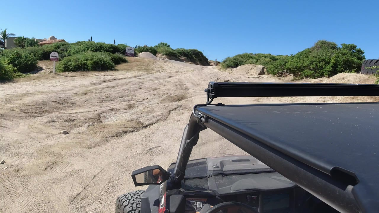 Sandy dirt road ahead of an off-road vehicle under a clear blue sky.