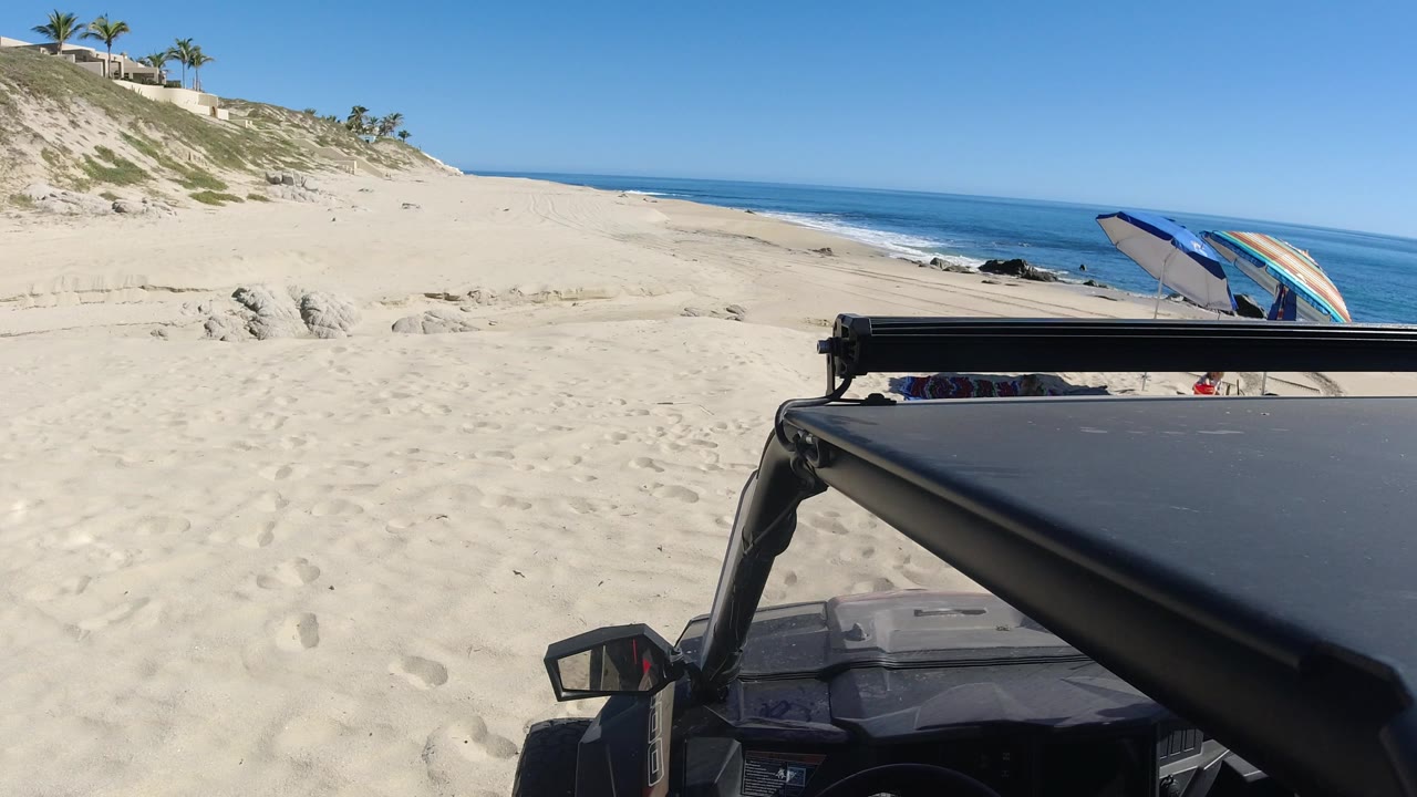 Parked Jeep beside a sandy beach with ocean in the background.