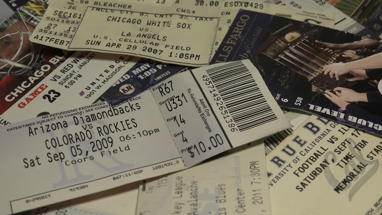 A close view centers on a baseball ticket among other layered admission stubs, with barcodes, section numbers, and no visible people.