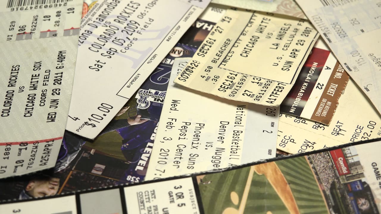 Close tabletop view of layered game tickets showing bleacher sections, row and seat information, prices, and repeated printed graphics, with no visible live people in the room.