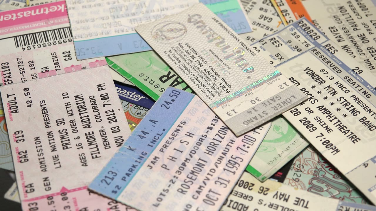 Overlapping tickets include blue parking sections, white admission stubs, green passes, and several visible printed listings across the paper pile, with no visible people.