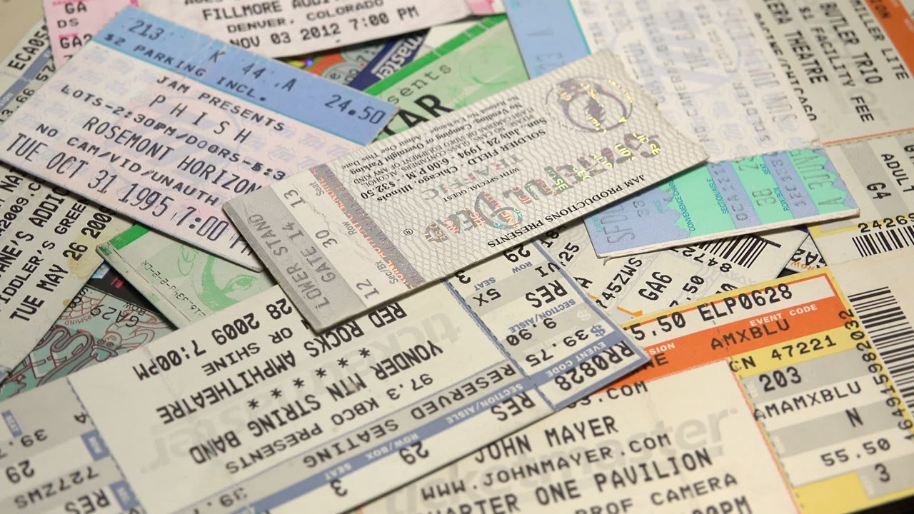 A close overhead view of assorted concert ticket stubs with barcodes, seat numbers, pastel paper, and no visible people.