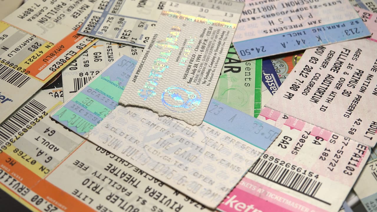 A close view of layered event tickets with barcodes, seat details, and pale blue and green stubs spread across the frame, with no visible people.