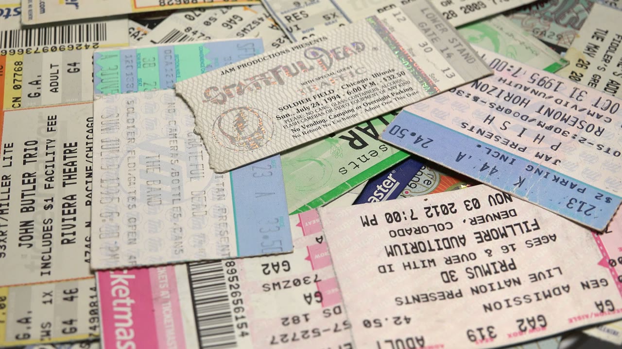 Layered tickets and worn stubs cover the frame, with faded printing, holographic marks, and pink, blue, and green accents visible among the paper, with no visible people.