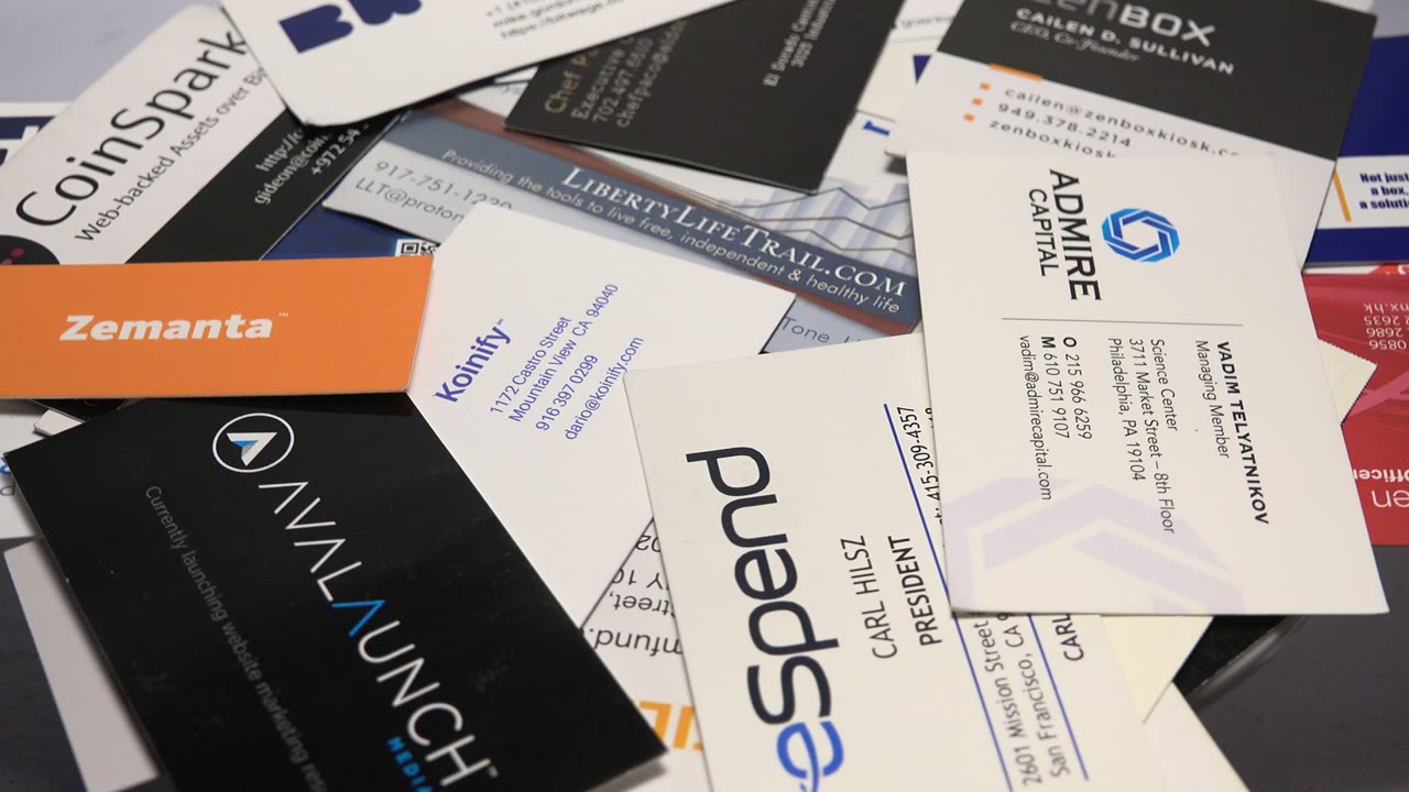 The second frame keeps the pile of calling cards tight in view, with a large white eSpend card, orange Zemanta card, black AnyLaunch card, and readable contact text, with no visible people.