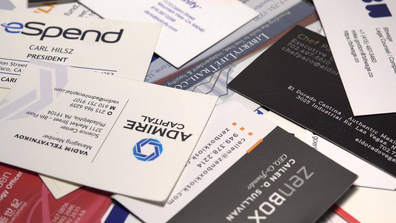 Close view of overlapping business cards and promotional mail with white, black, blue, and red printed pieces filling the frame, no visible people.