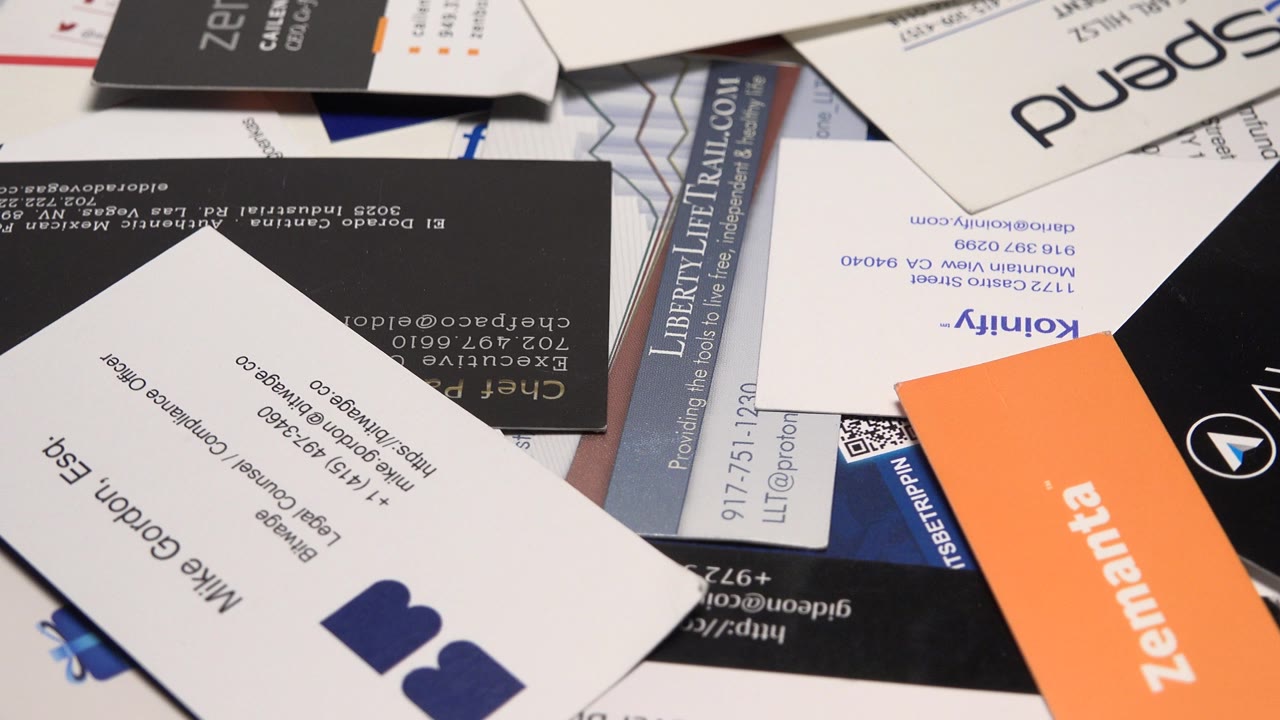 A close tabletop view of overlapping business cards with white, black, orange, and blue designs, including visible logos and contact text, with no visible people.