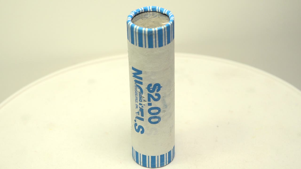 The wrapped roll of nickels is shown from another side on the white turntable, with vertical blue lettering and no visible people.