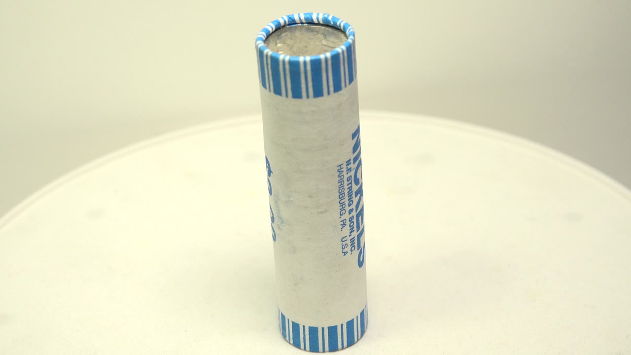 The upright roll of nickels is shown from a slightly different rotation, with side wrapper text partly visible against the same white board and no visible people.