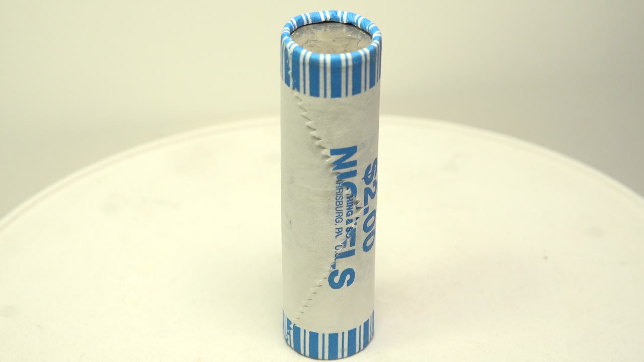 The wrapped nickel roll stands on the white surface with more of its side text angled away, the blue striped top still clear, and no visible people.