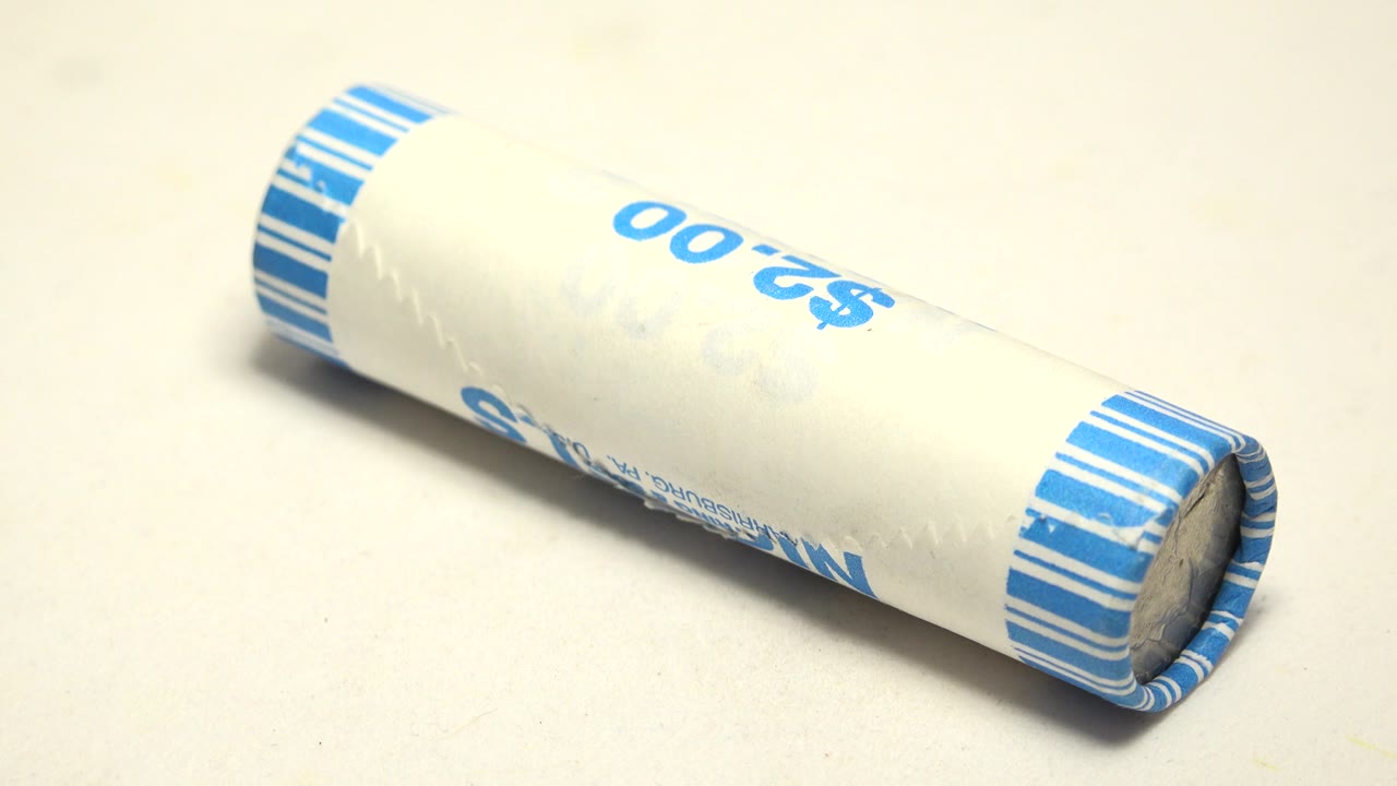 A white tube lies more horizontally across the pale surface, with blue striped bands at both ends and the $2.00 marking partly visible, with no visible people.