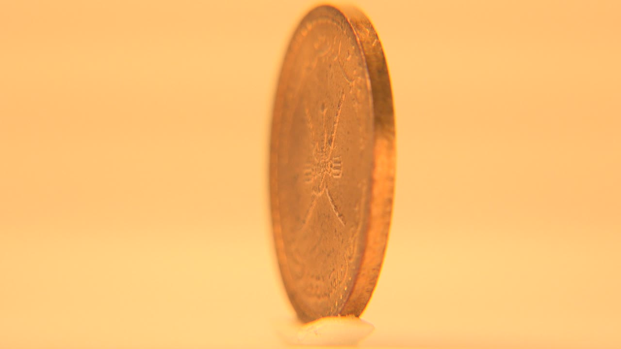 Gold coin on edge with warm light on a plain background.
