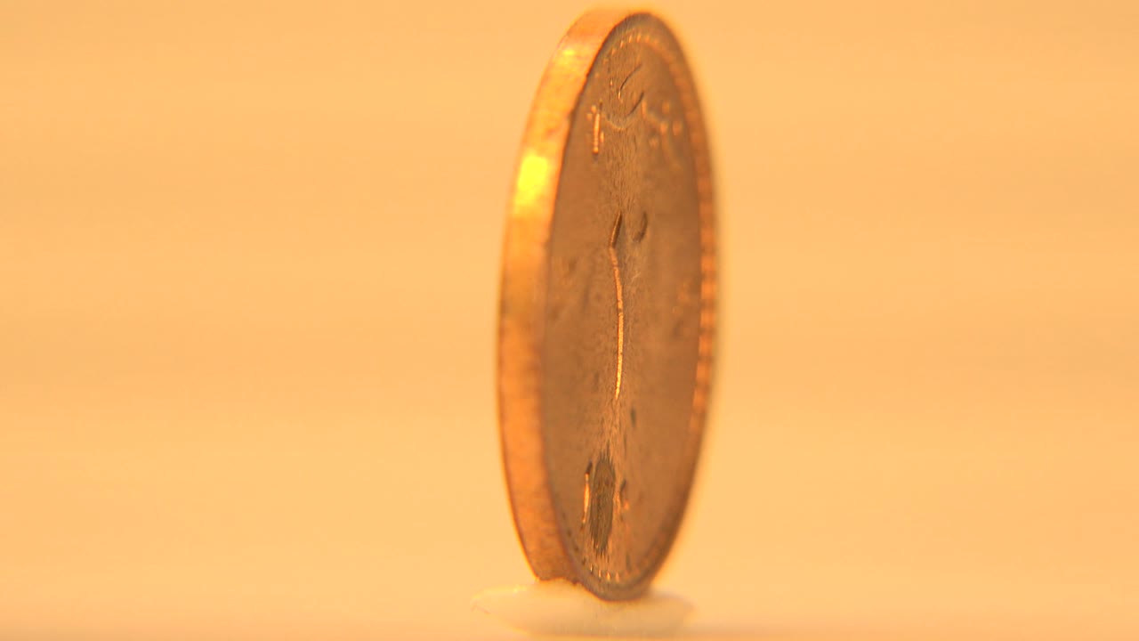 The coin is angled partly toward camera, showing a thin face and bright edge highlight against the warm cream-white field, with no visible people.