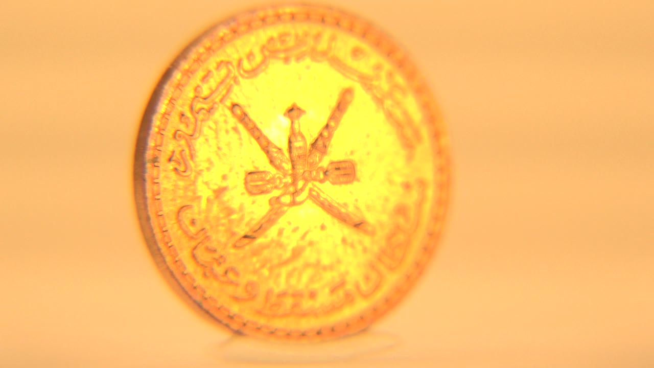 The coin remains centered in a bright face-on view, with its raised rim, central crossed emblems, Arabic lettering, and no visible people softened by golden exposure bloom.