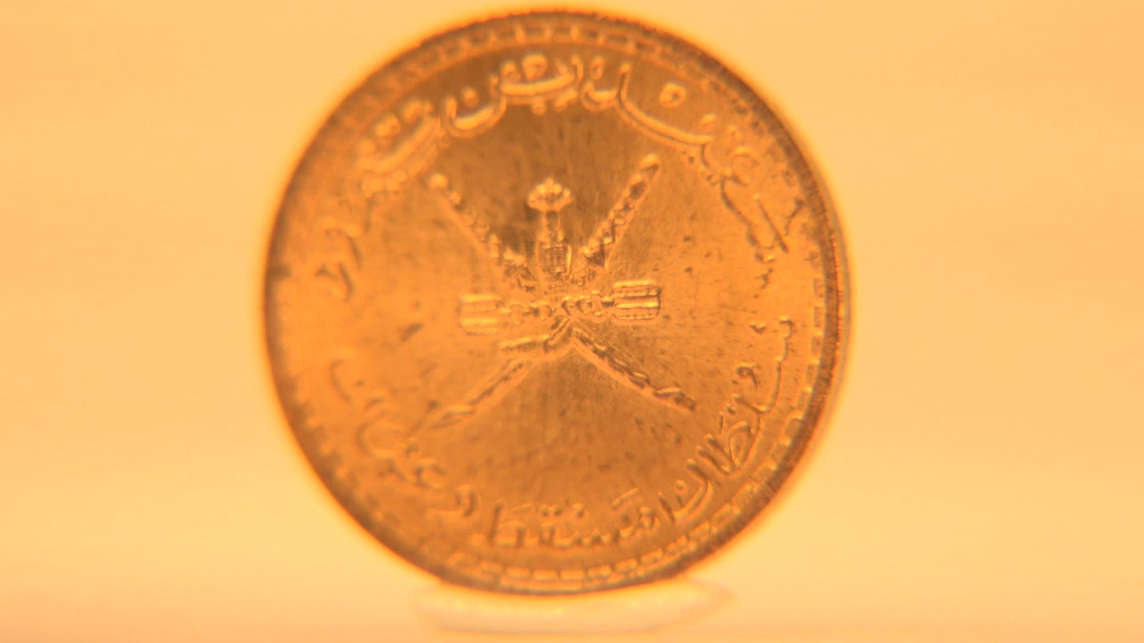 Darker upright coin face with Arabic script and central emblem.