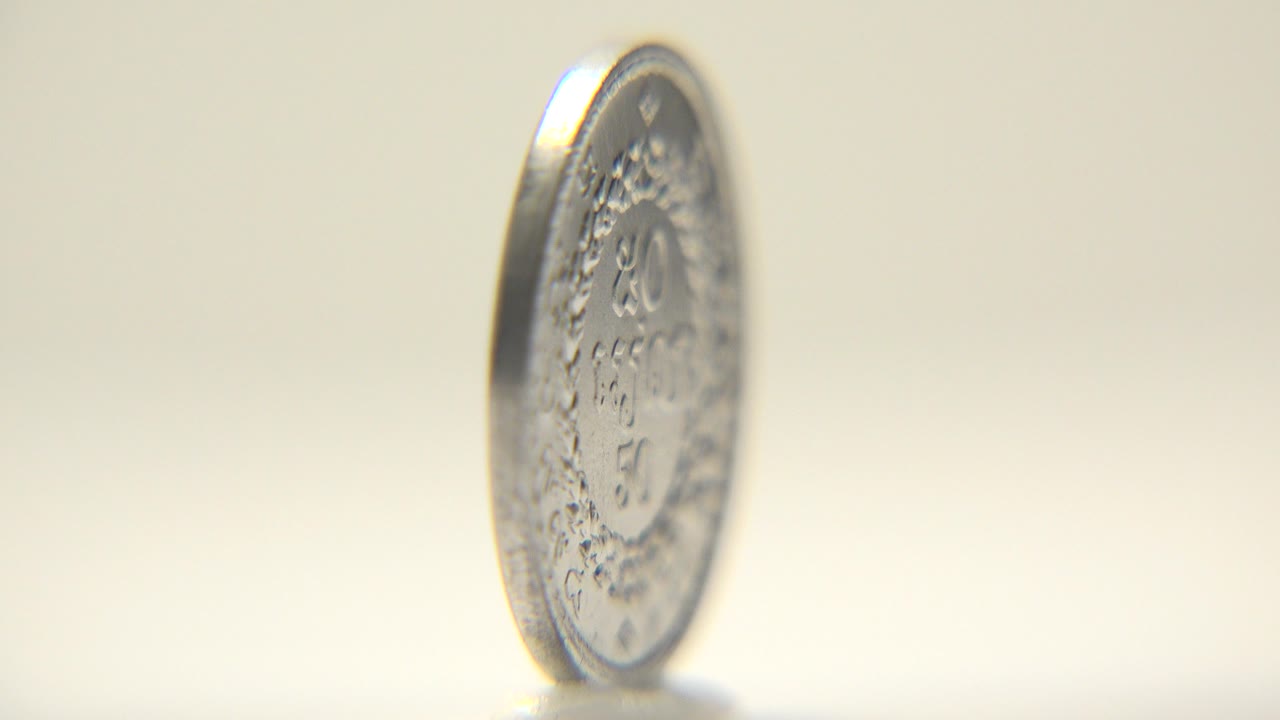 At the start, an upright silver coin is angled left of camera with engraved markings softened by shallow focus and no visible people.