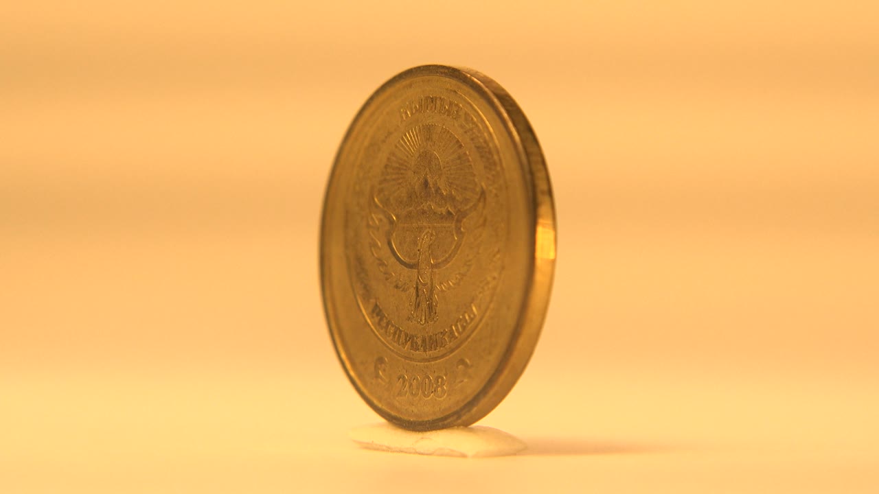 The rotating coin is angled to the right, showing a narrow edge and a dim partial face against the amber background, no visible people.