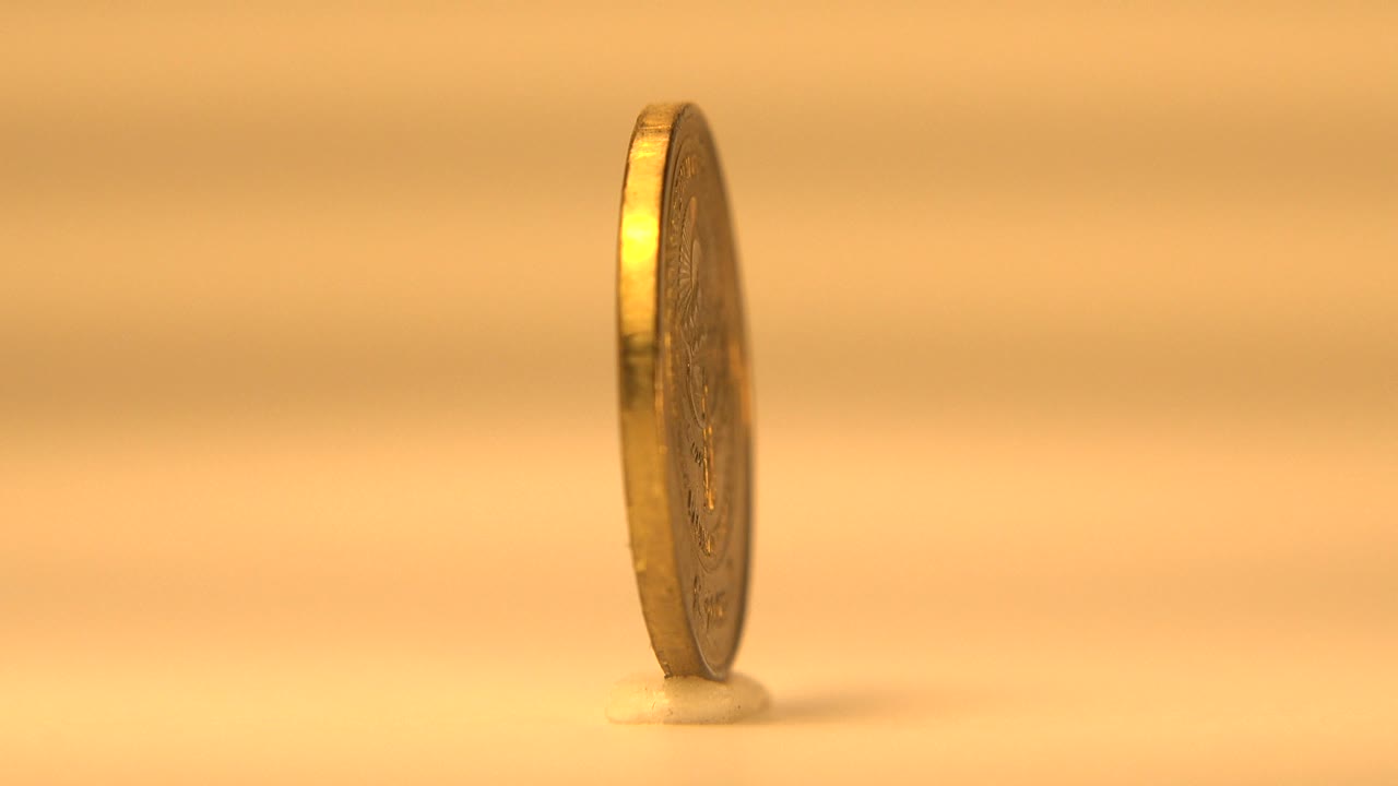 Gold-colored coin seen nearly edge-on against a yellow background.