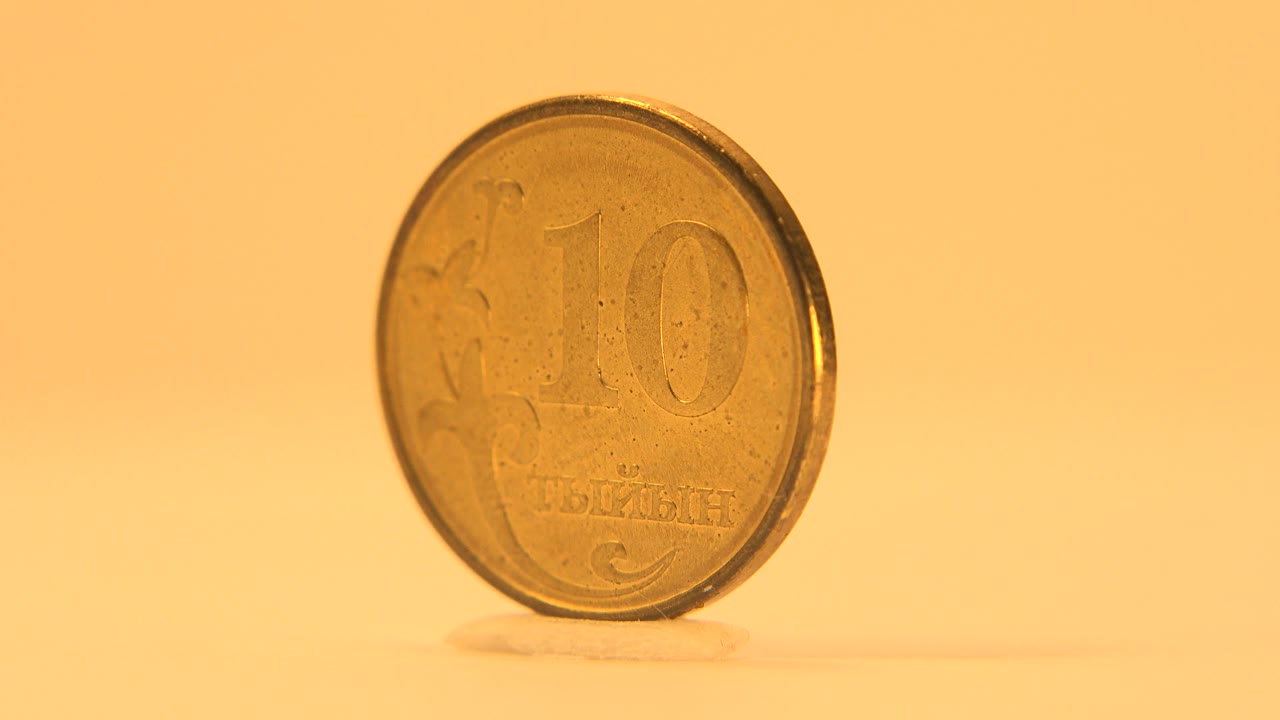 The coin remains upright and nearly front-facing, with the 10 marking visible through warm, slightly soft focus and no visible people.