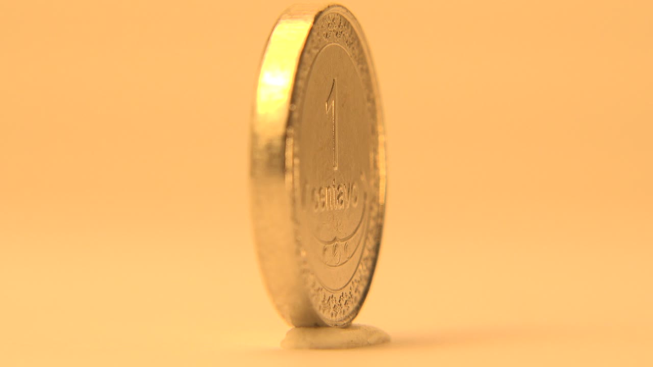 A Timor-Leste centavo coin stands upright in side profile on a pale surface with warm orange light and no visible people.