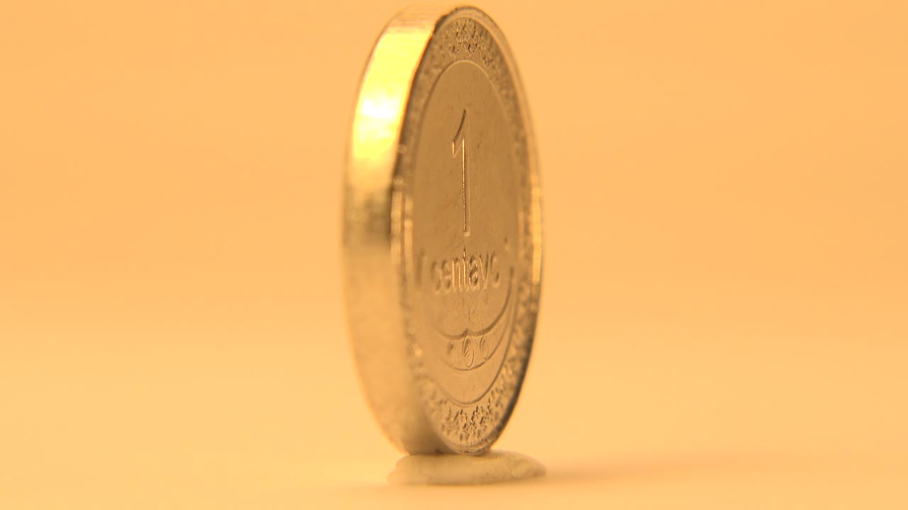 The coin remains upright in a narrow side angle, with its embossed face barely visible through shallow focus and no visible people.