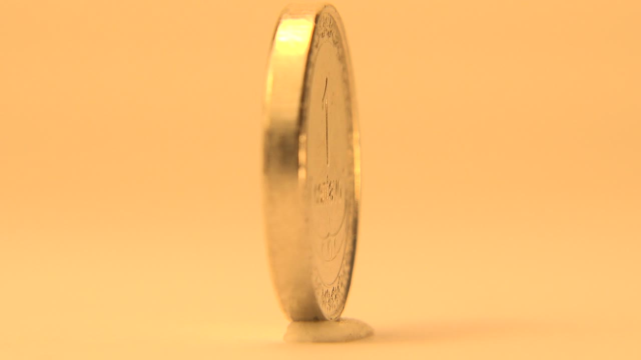 Thin side view of an upright coin on a warm yellow tabletop.