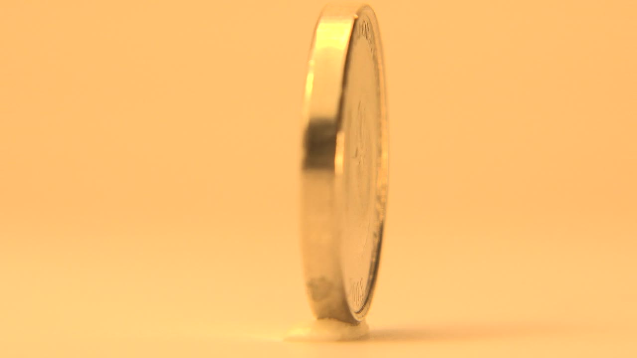 Upright coin seen from its thin edge on a warm orange background.