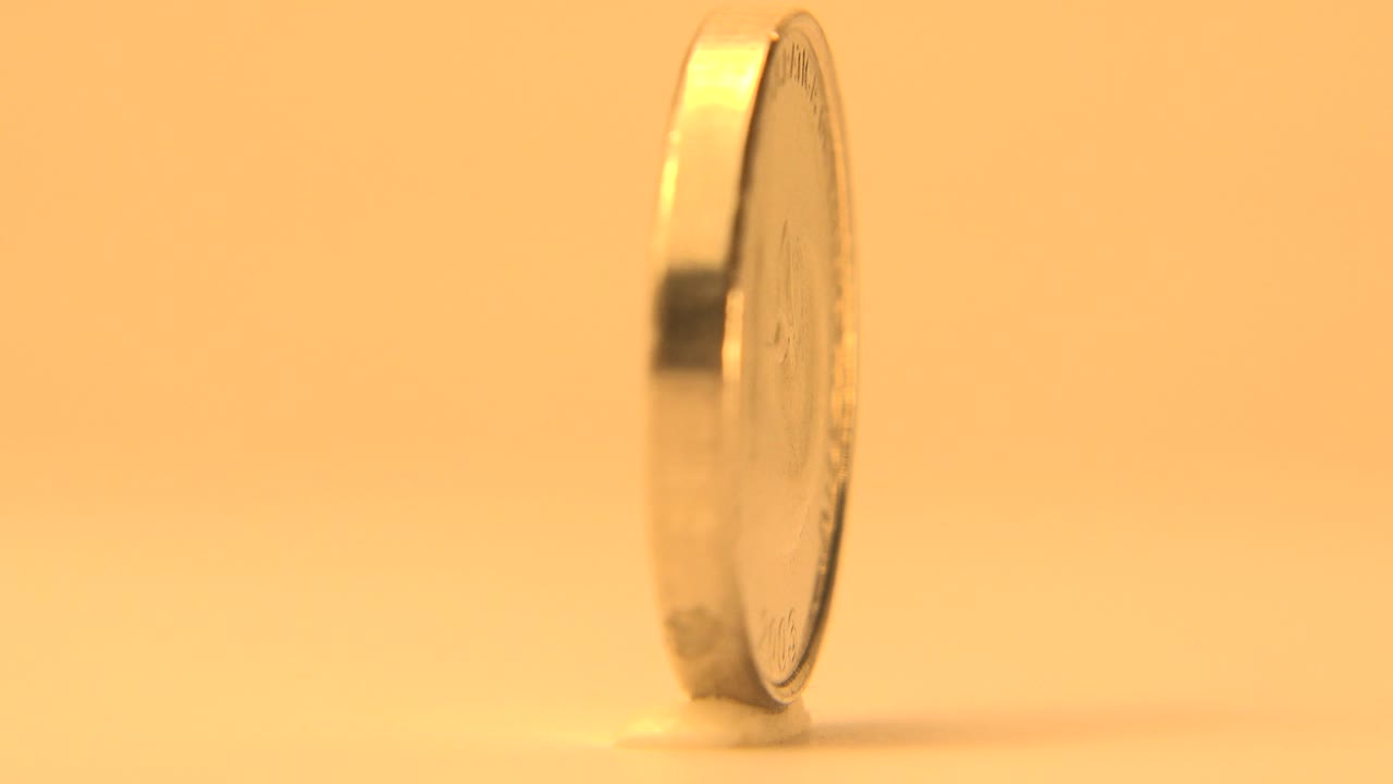 At 0:01, the coin remains upright in a narrow side view, with the round face largely hidden and no visible people.