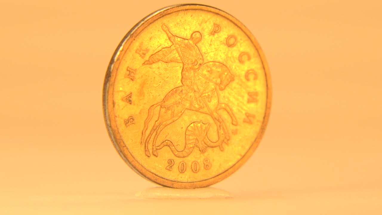 A brass-colored Russian coin stands upright with Saint George visible on the face and no visible people.