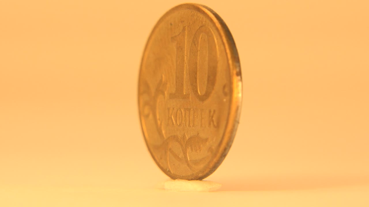 The golden coin remains upright and begins turning away from the front view, with its embossed 10 kopek face still partly visible and no visible people.