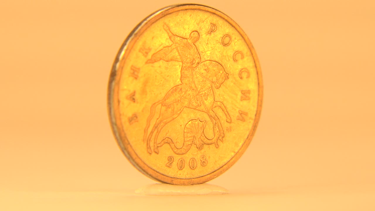 The reverse side of the golden coin faces the camera, showing a rider design and 2006 date on the coin against a warm orange background, with no visible people.
