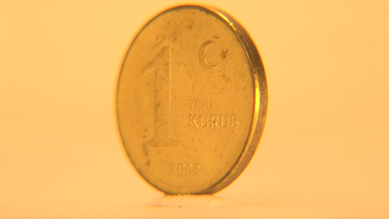 A small coin marked 1 Yeni Kurus stands upright facing the camera on a pale surface under warm yellow light, with no visible people.