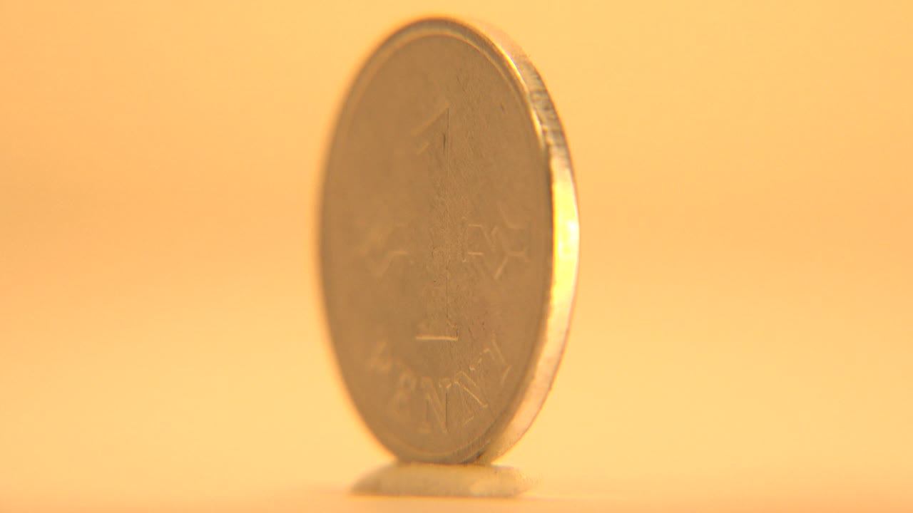 The coin has rotated into a thin edge profile near the right side of the frame, with rim highlights and no visible people.