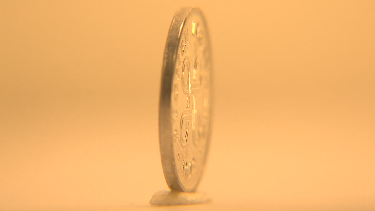 Coin in a thin side view on a pale surface with warm light.