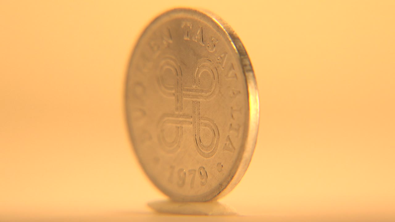 The coin is angled toward its thin edge while the front lettering remains faintly visible in warm light, with no visible people.