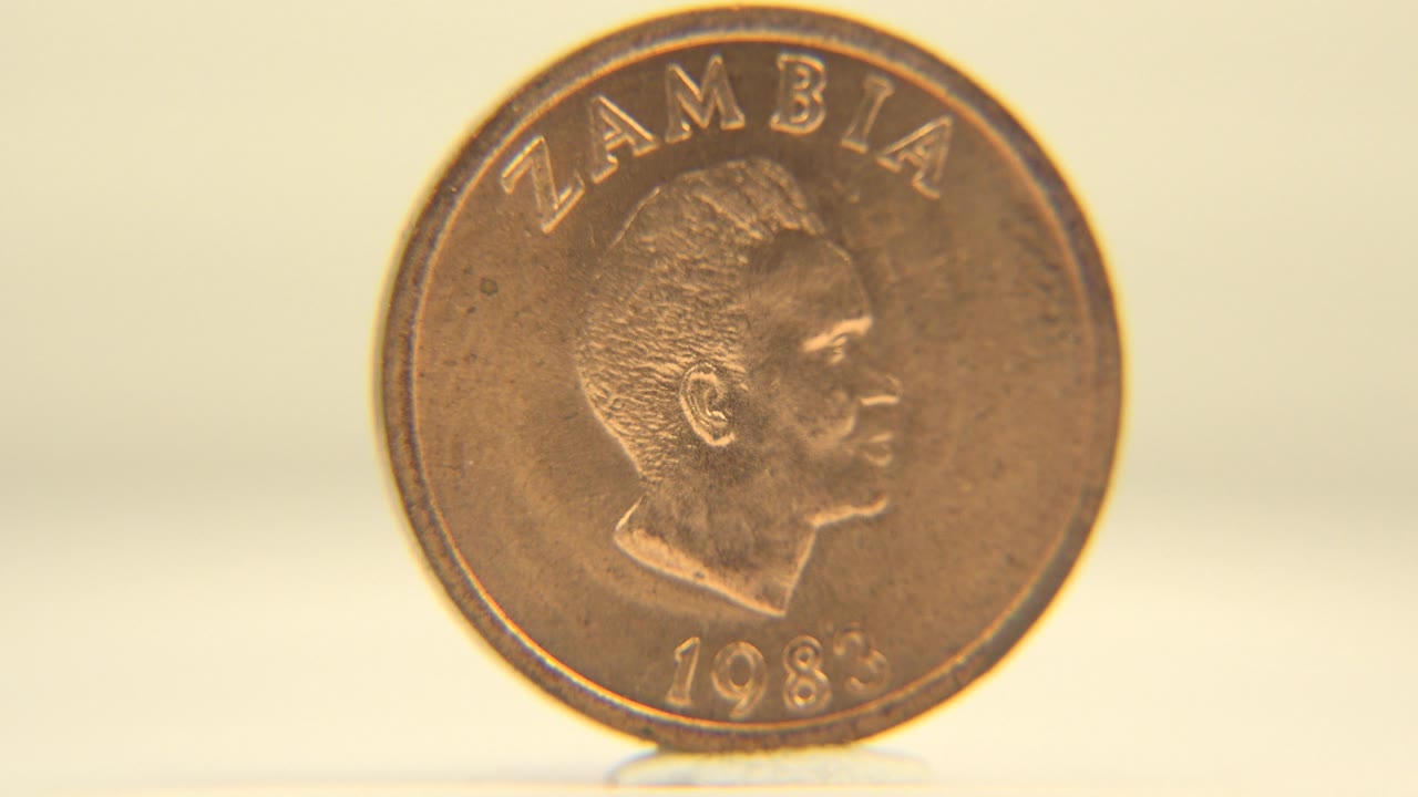 The coin faces the camera more directly, showing Zambia text, a portrait relief, and a 1983 date on a warm white background, no live people visible.